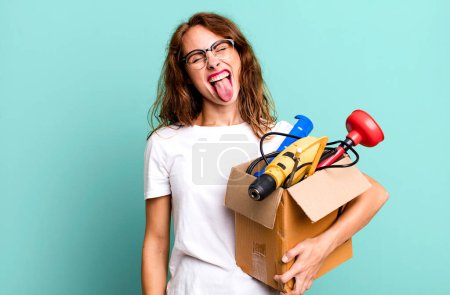 Foto de Mujer bonita hispana con actitud alegre y rebelde, bromeando y sacando la lengua con una caja de herramientas. concepto de manitas - Imagen libre de derechos