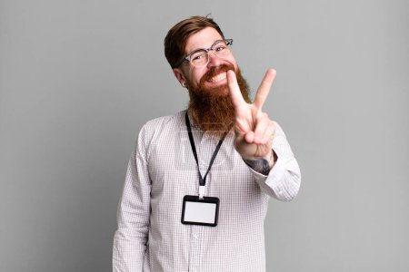 Foto de Barba larga hombre sonriendo y mirando feliz, señalando la victoria o la paz. concepto de acreditación vip badge - Imagen libre de derechos