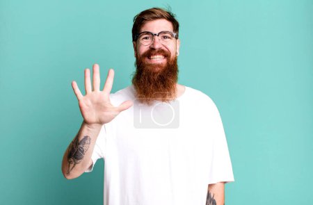 Téléchargez les photos : Barbe longue et cheveux roux homme souriant et regardant amical, montrant numéro cinq - en image libre de droit