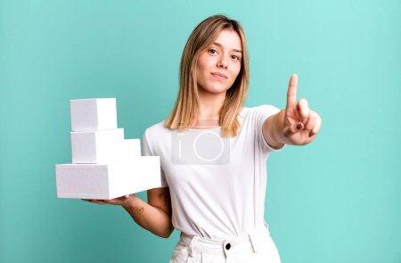 Photo for Young pretty woman smiling and looking friendly, showing number one. blank white boxes concept - Royalty Free Image