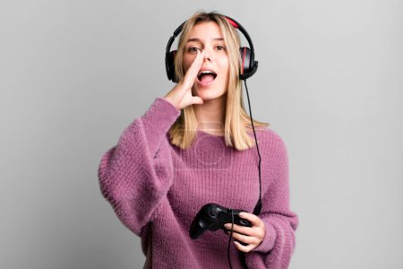 Photo for Young pretty woman feeling happy,giving a big shout out with hands next to mouth. gamer with headset and controller - Royalty Free Image