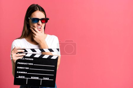Photo for Young pretty woman with mouth and eyes wide open and hand on chin. cinema film or movie concept - Royalty Free Image