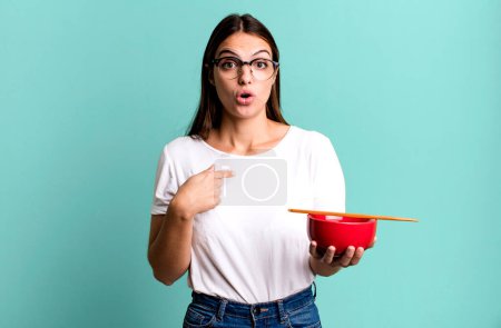 Photo for Young pretty woman looking shocked and surprised with mouth wide open, pointing to self. japanese ramen noodles concept - Royalty Free Image