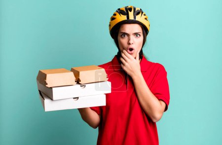 Foto de Young pretty woman with mouth and eyes wide open and hand on chin. pizza delivery concept - Imagen libre de derechos