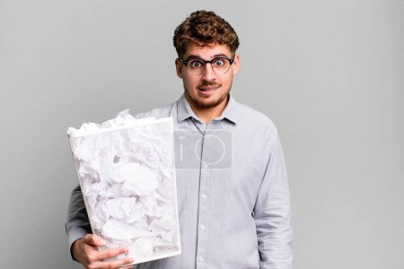 Téléchargez les photos : Jeune homme caucasien adulte regardant perplexe et confus avec un concept de poubelle boules de papier - en image libre de droit