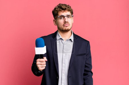 Photo for Young adult caucasian man feeling sad and whiney with an unhappy look and crying. journalist or presenter with a microphone - Royalty Free Image