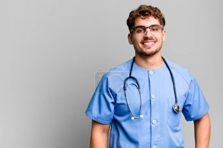 Foto de Joven hombre caucásico adulto sonriendo felizmente con una mano en la cadera y confiado. concepto de enfermera - Imagen libre de derechos
