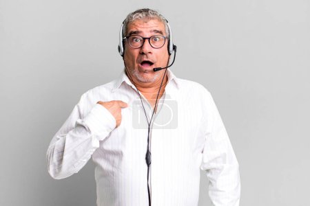 Photo for Middle age senior man looking shocked and surprised with mouth wide open, pointing to self. telemarketer or client attention agent concept - Royalty Free Image