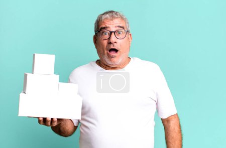 Foto de Hombre mayor de mediana edad que parece muy sorprendido o sorprendido. cajas en blanco de diferentes paquetes - Imagen libre de derechos