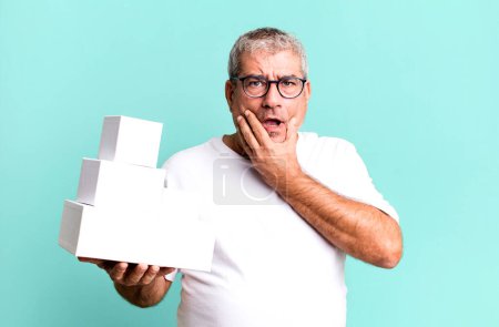 Photo for Middle age senior man with mouth and eyes wide open and hand on chin. different packages blank boxes - Royalty Free Image