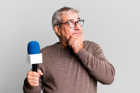 Foto de Hombre mayor de mediana edad pensando, sintiéndose dudoso y confundido. periodista o presentador de televisión con un micro - Imagen libre de derechos