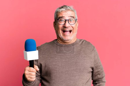 Photo for Middle age senior man looking happy and pleasantly surprised. journalist or tv presenter with a micro - Royalty Free Image