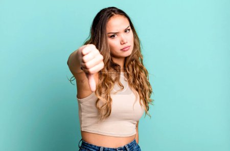 Photo for Young pretty woman feeling cross, angry, annoyed, disappointed or displeased, showing thumbs down with a serious look - Royalty Free Image