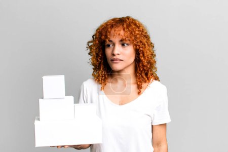 Photo for Red hair pretty woman feeling sad, upset or angry and looking to the side. blank packages boxes concept - Royalty Free Image