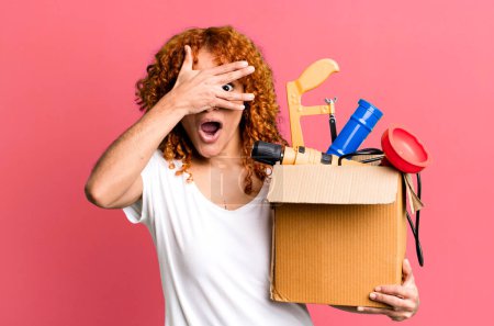 Photo for Red hair pretty woman looking shocked, scared or terrified, covering face with hand. housekeeper and toolbox concept - Royalty Free Image