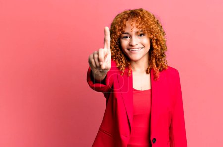 Photo for Red hair pretty woman smiling and looking friendly, showing number one. businesswoman concept - Royalty Free Image