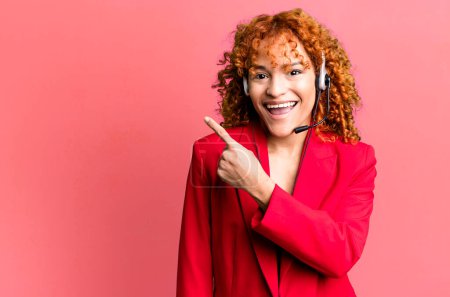 Photo for Red hair pretty woman looking excited and surprised pointing to the side. telemarketing concept - Royalty Free Image