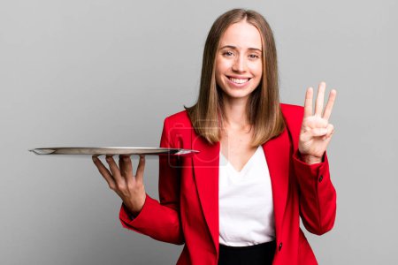 Photo for Smiling and looking friendly, showing number three. businesswoman presenting with a tray - Royalty Free Image
