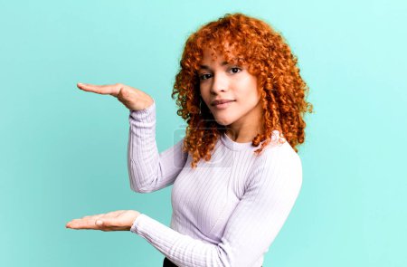 Photo for Redhair pretty woman holding an object with both hands on side copy space, showing, offering or advertising an object - Royalty Free Image