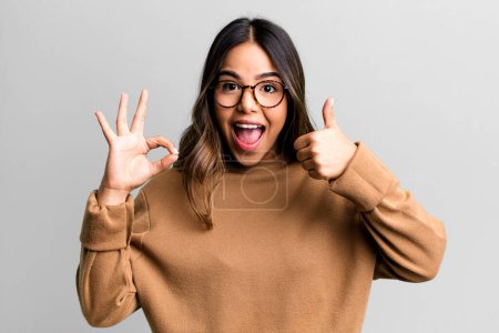 Photo for Hispanic pretty woman feeling happy, amazed, satisfied and surprised, showing okay and thumbs up gestures, smiling - Royalty Free Image