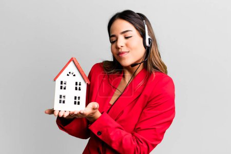 Foto de Hispanic pretty young adult woman real state agent with a house model and headset - Imagen libre de derechos