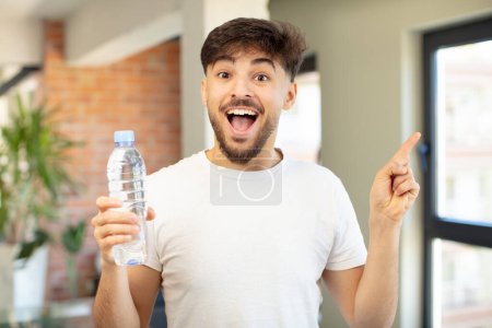 Téléchargez les photos : Jeune homme beau se sentant comme un génie heureux et excité après avoir réalisé une idée. concept de bouteille d'eau - en image libre de droit