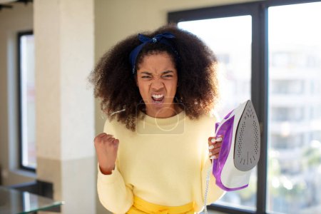 Foto de Mujer negra bastante afro buscando enojado, molesto y frustrado. ropa de hierro concepto de lavandería - Imagen libre de derechos