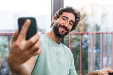 Téléchargez les photos : Jeune homme barbu fou adulte avec un smartphone. vue intérieure - en image libre de droit