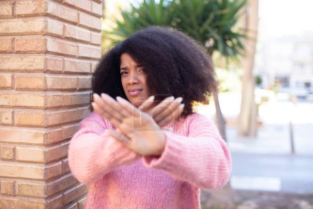 Foto de Africano americana bonita mujer cubriendo la cara con la mano y poniendo otra mano por delante para detener la cámara, negando fotos o imágenes - Imagen libre de derechos
