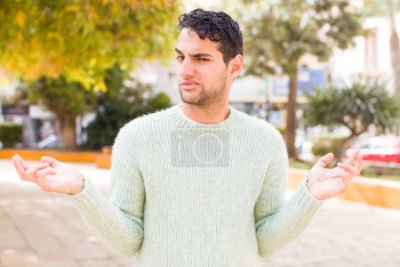 Photo for Young hispanic man looking puzzled, confused and stressed, wondering between different options, feeling uncertain - Royalty Free Image