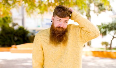 Photo for Red hair bearded man feeling puzzled and confused, scratching head and looking to the side - Royalty Free Image