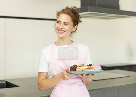 Foto de Young pretty woman smiling with a happy, confident expression with hand on chin. home made cakes concept - Imagen libre de derechos