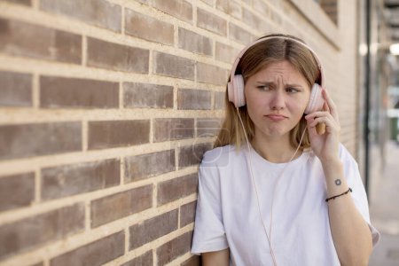 Photo for Young pretty woman feeling sad and whiney with an unhappy look and crying. headphones and music concept - Royalty Free Image