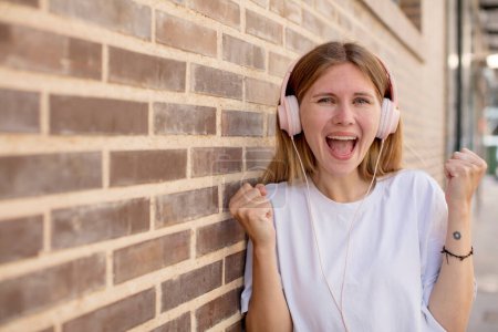 Foto de Joven bonita mujer sintiéndose sorprendida, riendo y celebrando el éxito. auriculares y concepto de música - Imagen libre de derechos