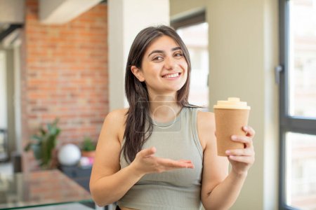 Téléchargez les photos : Jeune femme souriant joyeusement, se sentant heureuse et montrant un concept. emporter café - en image libre de droit