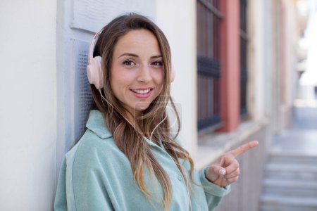 Foto de Bonita mujer sonriendo alegremente, sintiéndose feliz y señalando hacia un lado. auriculares y concepto de música - Imagen libre de derechos