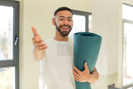 Téléchargez les photos : Homme beau arabe homme arabe souriant heureux et offrant ou montrant un concept. yoga concept mat - en image libre de droit
