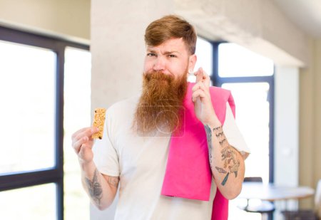 Photo for Red hair man crossing fingers and hoping for good luck with a cereal bar. fitness concept - Royalty Free Image