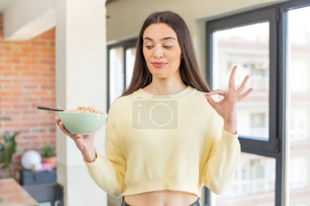 Photo for Pretty young model feeling happy, showing approval with okay gesture. breakfast bowl concept - Royalty Free Image