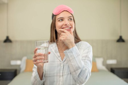 Foto de Joven mujer bonita sonriendo con una expresión feliz y segura con la mano en la barbilla. concepto de vidrio de agua - Imagen libre de derechos