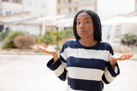 Foto de Afro bonita mujer negra sintiéndose perpleja y confundida, dudando, ponderando o eligiendo diferentes opciones - Imagen libre de derechos