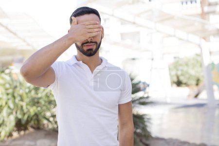 Photo for Young handsome man covering eyes with one hand feeling scared or anxious, wondering or blindly waiting for a surprise - Royalty Free Image