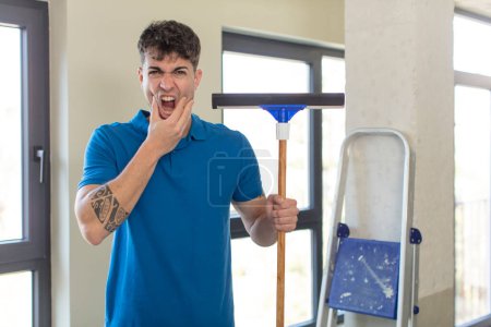 Photo for Young handsome man with mouth and eyes wide open and hand on chin. windows washer concept - Royalty Free Image