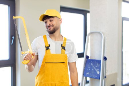 Photo for Young handsome man smiling and looking with a happy confident expression. handyman with a saw - Royalty Free Image