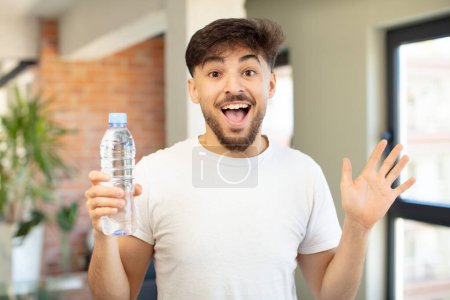 Téléchargez les photos : Jeune homme beau se sentant heureux et étonné de quelque chose d'incroyable. concept de bouteille d'eau - en image libre de droit
