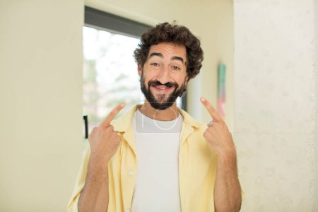 Téléchargez les photos : Jeune homme barbu fou souriant avec confiance pointant vers son propre sourire large, attitude positive, détendue, satisfaite - en image libre de droit