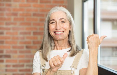Téléchargez les photos : Senior jolie femme souriant joyeusement et décontracté pointant vers copier l'espace sur le côté, se sentant heureux et satisfait - en image libre de droit