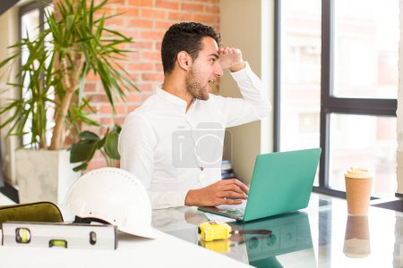 Photo for Young hispanic man looking bewildered and astonished, with hand over forehead looking far away, watching or searching. architect concept - Royalty Free Image