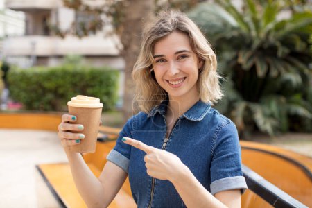 Photo for Pretty woman smiling cheerfully, feeling happy and pointing to the side. take away coffee concept - Royalty Free Image