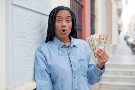 Photo for Black afro woman feeling extremely shocked and surprised. dollar banknotes concept - Royalty Free Image